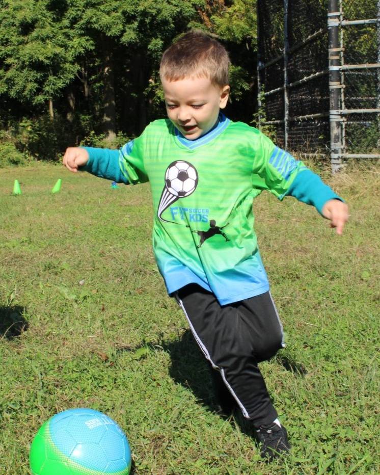 Two young Fit Soccer Kids players in green jerseys running after a soccer ball on a grass field