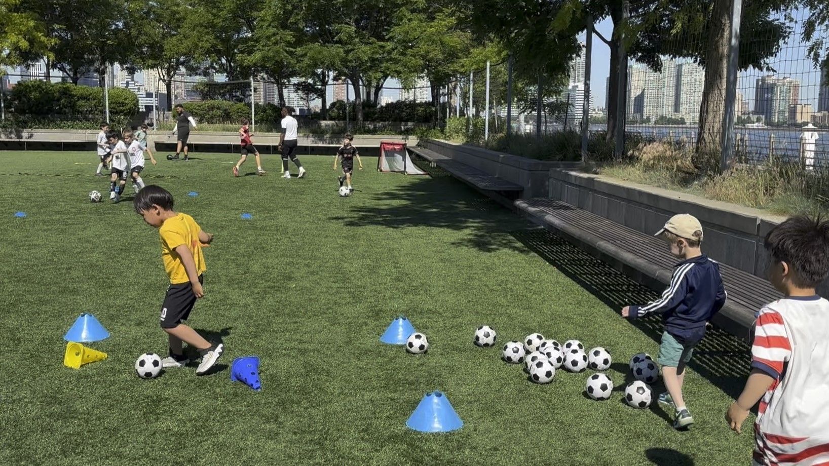 Two young Fit Soccer Kids players dribbling soccer balls with the Manhattan skyline in the background