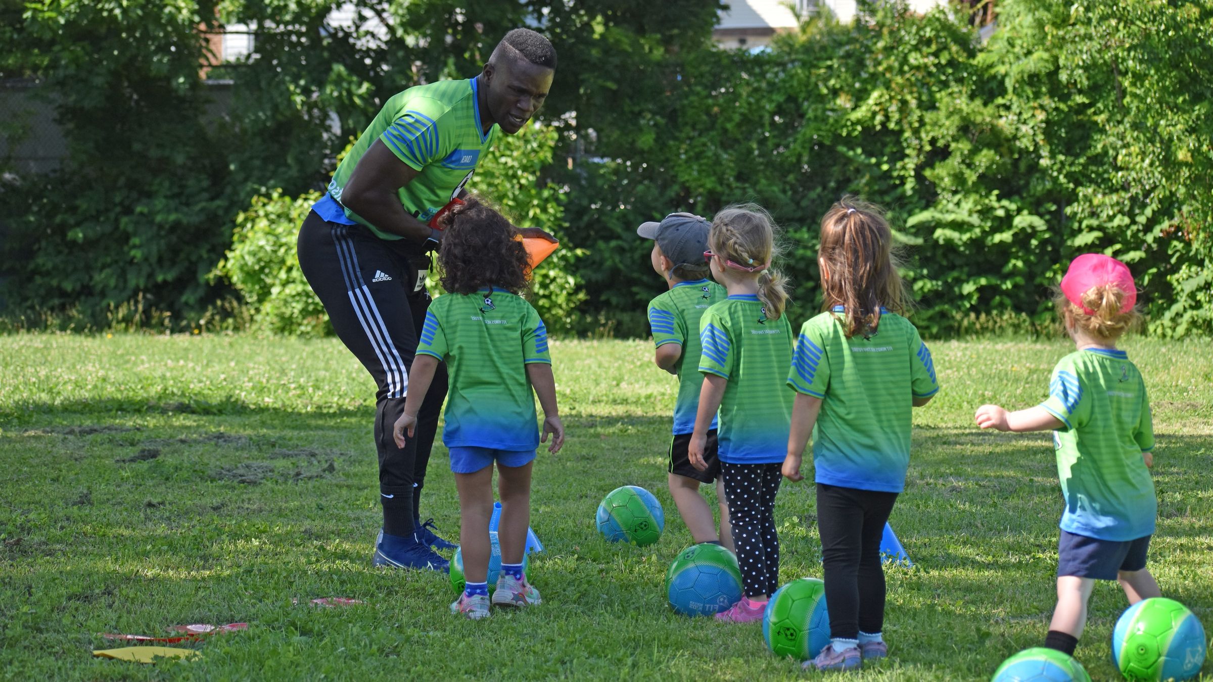 Fit Soccer Kids coach and children in green jerseys during an outdoor class session in the park