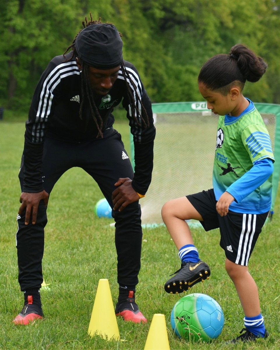 Fit Soccer Kids coach kneeling to guide a young player through a dribbling skill move