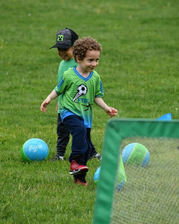 Young Fit Soccer Kids player smiling while dribbling a soccer ball in the park