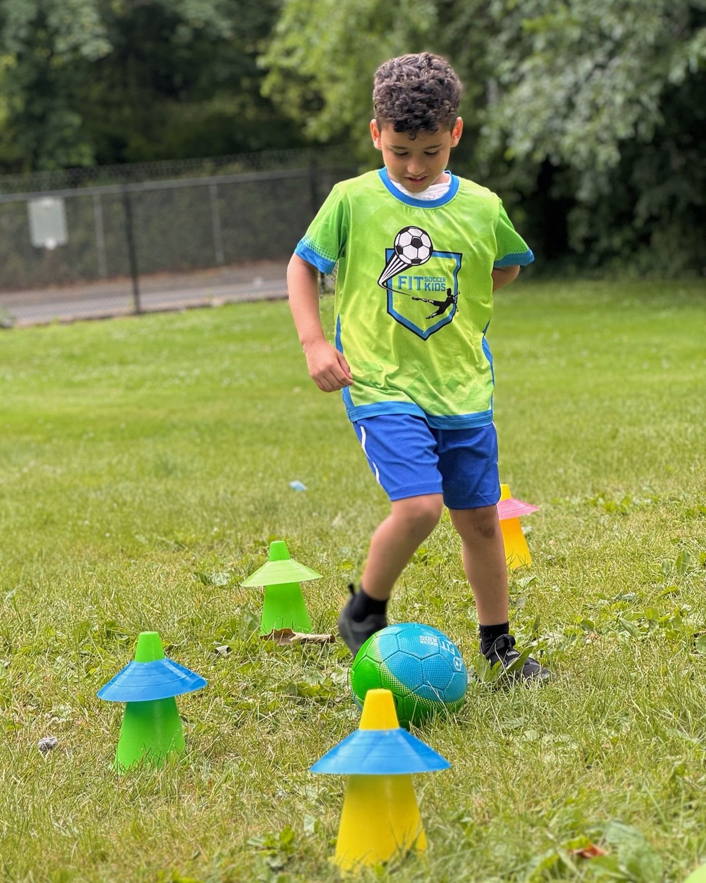 Young Fit Soccer Kids player dribbling a soccer ball through cone markers
